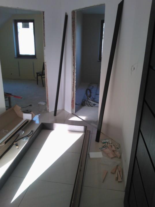 Montaż ościeżnic drzwiowych w trakcie wykończenia wnętrza w Sosnowcu. Widoczne elementy ościeżnic i narzędzia na podłodze z płytek.