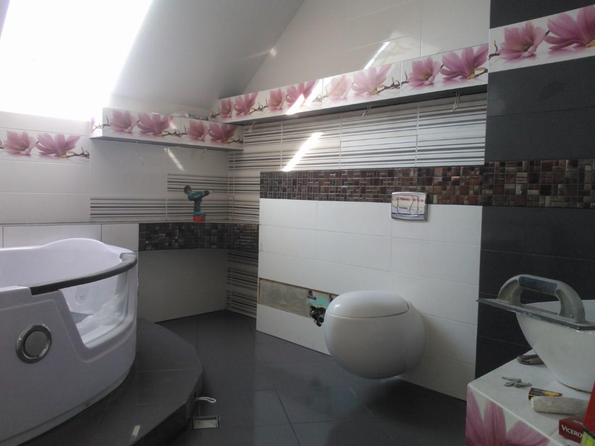 Nowoczesna łazienka w trakcie wykańczania z wanną jacuzzi, wiszącą toaletą i dekoracyjnymi płytkami z motywem kwiatowym. Widoczny sprzęt glazurniczy.