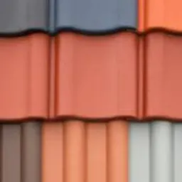 Bliskie ujęcie fragmentu dachu z ułożonymi obok siebie dachówkami w różnych kolorach: szarym, ceglastym, brązowym i białym. Dachówki mają falisty kształt.