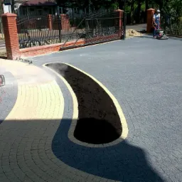 Pracownik przycina kostkę granitową szlifierką kątową podczas budowy podjazdu z dekoracyjnym wzorem i miejscem na rośliny.