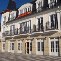 Elewacja budynku z balkonami i oknami w stylu klasycystycznym, z widoczną kostką brukową na chodniku. Charakterystyczny element architektoniczny.