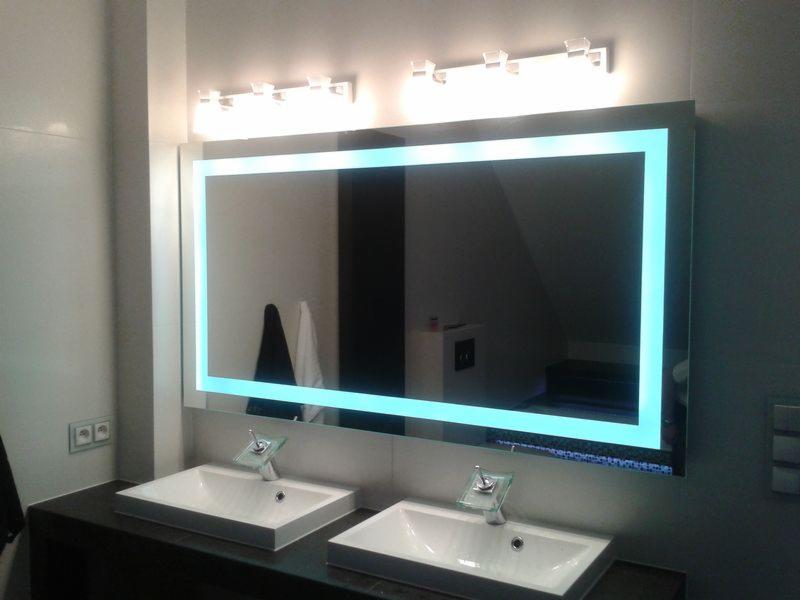 Nowoczesna łazienka z podświetlanym lustrem LED, dwie białe umywalki z chromowanymi bateriami, ciemny blat i jasne ściany.