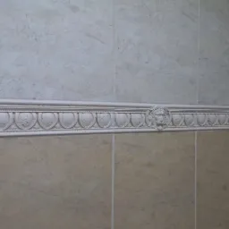 Beżowe płytki ścienne z dekoracyjnym, białym frezem z motywem lwa, oddzielającym górną i dolną część ściany. Klasyczne wykończenie łazienki.