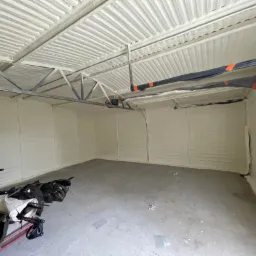 Wnętrze garażu po ociepleniu pianką PUR, widoczne równomierne pokrycie ścian i dachu, z pozostawionymi narzędziami i wózkiem na podłodze.