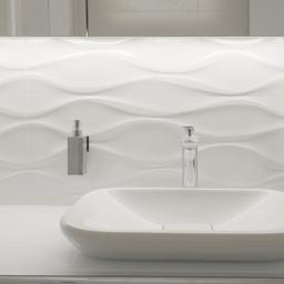 Niuans Projektowanie Wnętrz - Nowoczesna, biała łazienka z umywalką o geometrycznym kształcie, chromowaną baterią i dozownikiem mydła na tle falistych płytek ściennych podświetlonych LED.
