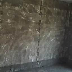 Surowe wnętrze w trakcie tynkowania: ściany pokryte grubą warstwą szarego tynku, widoczne pionowe listwy prowadzące, fragment ściany z pustaków oraz okno w prawym rogu.