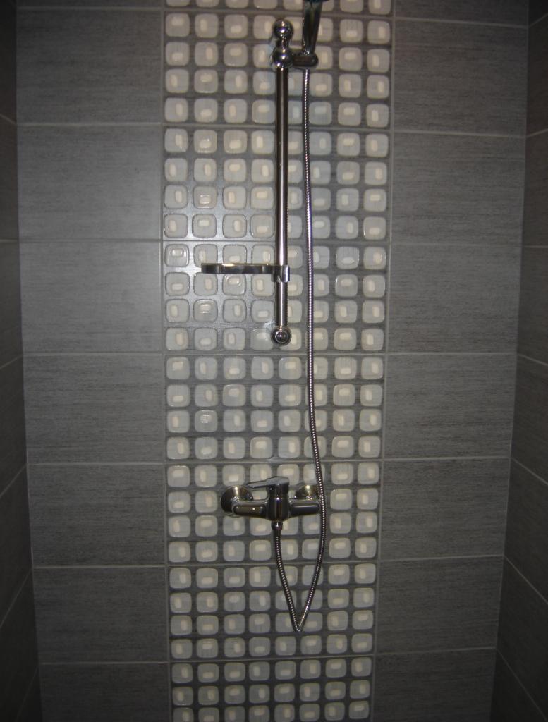 Szara łazienka z chromowaną armaturą prysznicową i dekoracyjną mozaiką kwadratową na ścianie. Minimalistyczny design.