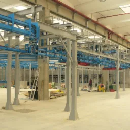 Montaż suwnicy przemysłowej w hali: stalowe słupy, niebieskie szyny transportowe, drabina oparta o filar. Prace spawalnicze w toku, widoczne materiały i narzędzia.