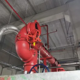 Czerwona instalacja przeciwpożarowa z zaworami motylkowymi i sterowaniem ręcznym, widoczna pod betonowym stropem budynku.