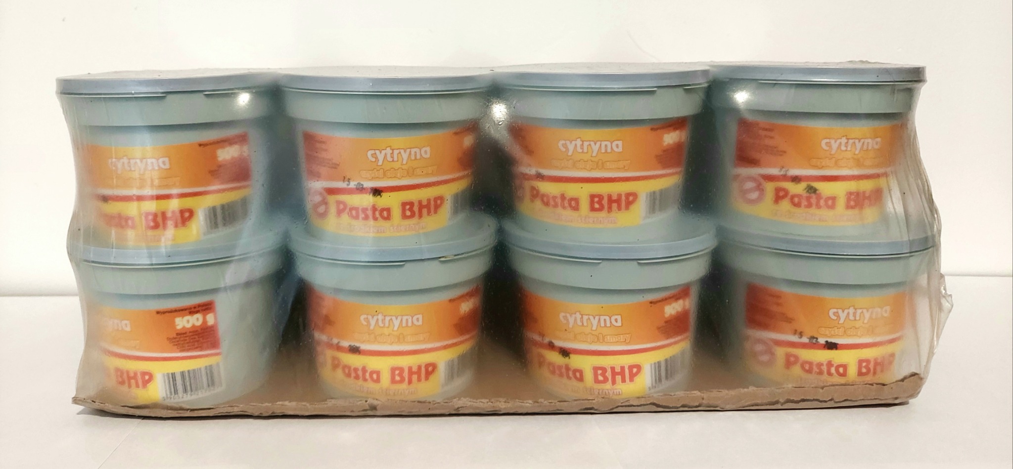 Osiem plastikowych pojemników z pastą BHP o zapachu cytrynowym, zapakowanych w folię termokurczliwą i umieszczonych w kartonowym pudełku.