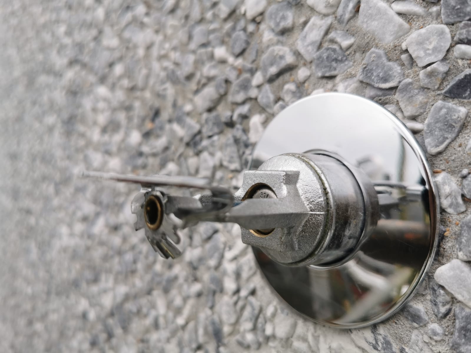 Zamknięty, srebrny zraszacz przeciwpożarowy zamontowany na szorstkiej, kamiennej ścianie.