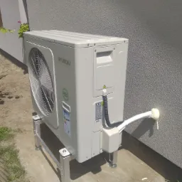 Zamontowana zewnętrzna jednostka pompy ciepła Hyundai na metalowym stelażu przy ścianie budynku z wyprowadzoną rurą, zabezpieczoną pianką montażową.