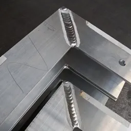 Połączenie spawane dwóch aluminiowych profili pod kątem prostym, widoczne ślady po procesie spawania i szlifowania.