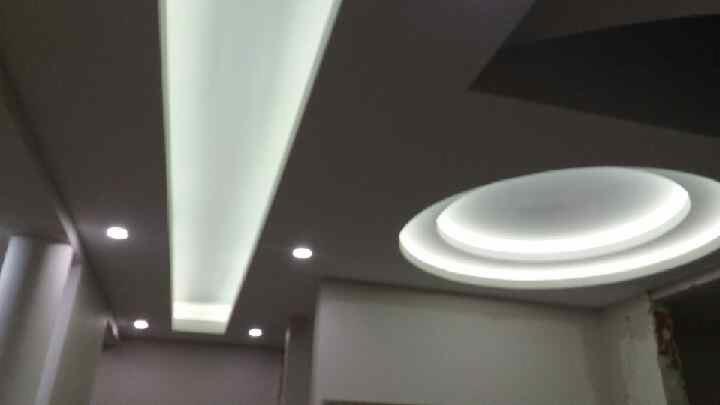 Nowoczesny sufit podwieszany z oświetleniem LED: podłużny panel świetlny i okrągła lampa sufitowa z dwoma pierścieniami świetlnymi.