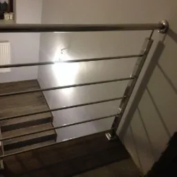 Schody wewnętrzne z balustradą ze stali nierdzewnej, widok z góry, minimalistyczny design.
