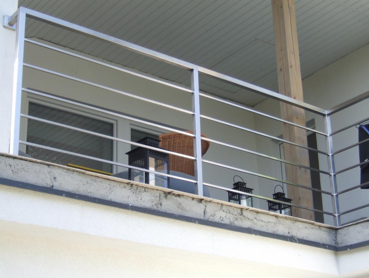 Nowoczesna, pozioma, metalowa balustrada balkonowa z widokiem na okno i dekoracje,  w jasnej tonacji, z drewnianym słupem wspierającym konstrukcję.