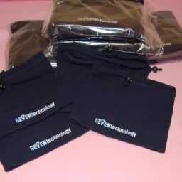 Stos niebieskich kominiarek z nadrukowanym logo SEVENtechnology, niektóre zapakowane w foliowe woreczki.