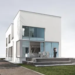 Wizualizacja nowoczesnego, białego domu z dużymi przeszkleniami, drewnianym tarasem i parą obejmującą się na nim.