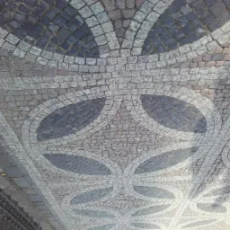 Wzór z kostki granitowej w odcieniach szarości, tworzący dekoracyjny motyw roślinny. Kąt ujęcia z góry podkreśla precyzję wykonania i unikalny design nawierzchni.