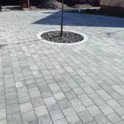 Ułożona szara kostka brukowa na podjeździe z dekoracyjnym okręgiem z kamieni wokół słupa oświetleniowego.