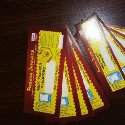 Stos wizytówek z logo pasieki miodu, z elementami graficznymi przedstawiającymi pszczołę i plaster miodu, ułożonych na ciemnym blacie.