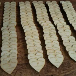 Rzędy drewnianych serduszek z wygrawerowanymi imionami i datami, układanka na drewnianym stole, pamiątka ślubna z magnesem.