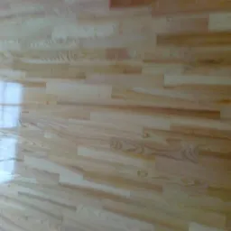 Jasne, lakierowane deski parkietu ułożone w regularny wzór, z refleksami światła okiennego. Widoczna struktura drewna i połyskliwa powierzchnia.