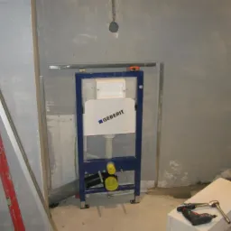 Stelaż podtynkowy Geberit zamontowany w surowej łazience, widoczne narzędzia i poziomica, ściany przygotowane pod wykończenie.