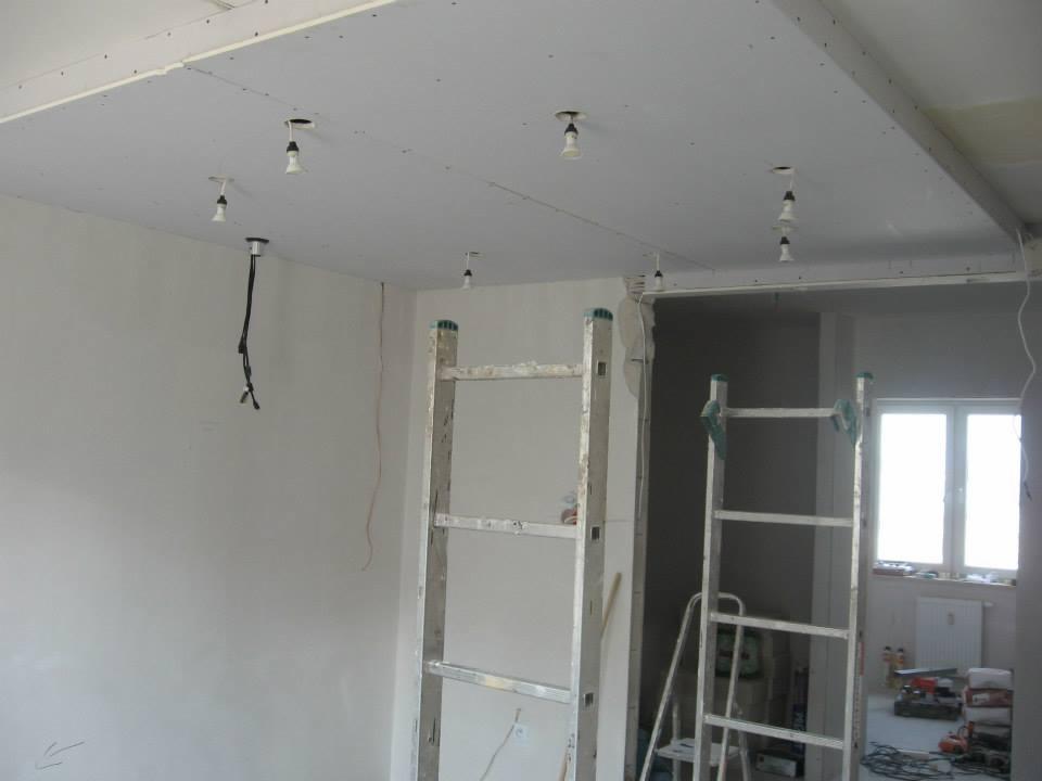Montaż sufitu podwieszanego z widocznymi punktami oświetleniowymi i drabina. Prace wykończeniowe w nowym mieszkaniu.