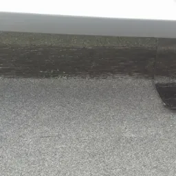 Szczegółowe ujęcie fragmentu dachu pokrytego papą, z wyraźnie widocznym połączeniem/uszczelnieniem na łączeniu, wykonanym czarną masą bitumiczną.