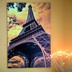 Fotoobraz przedstawiający wieżę Eiffla z perspektywy żabiej, wiszący na ścianie obok dekoracyjnych lampek.