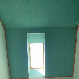 CENDRUS Michał Cendrowski - Montaż zielonej płyty gipsowo-kartonowej wokół okna dachowego, widoczne wkręty i taśmy narożnikowe. Etap prac wykończeniowych poddasza.