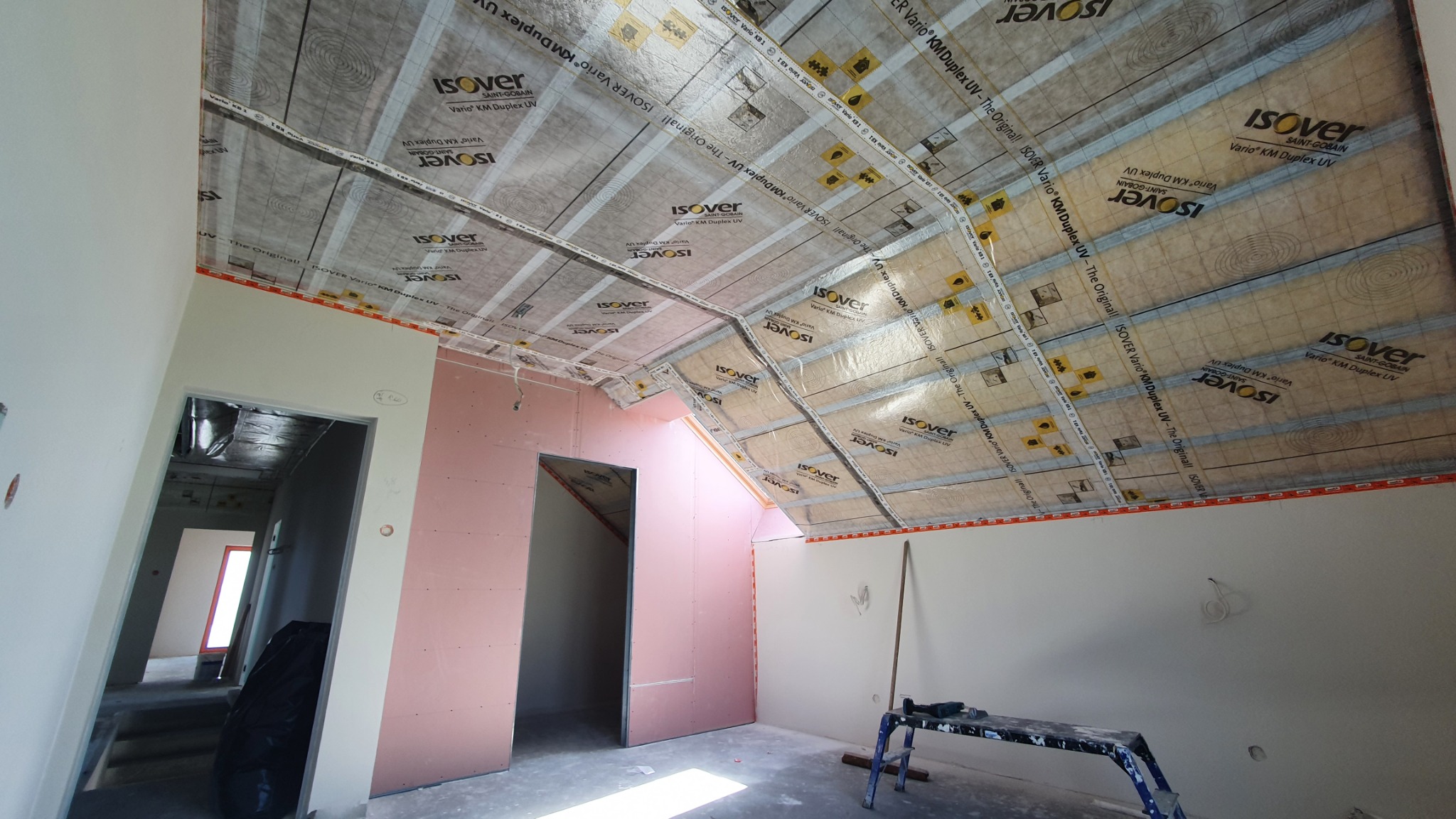 Poddasze w trakcie prac: widoczne płyty karton-gips na ścianach, izolacja na skośnym dachu, przewody elektryczne i drabina malarska. Etap wykończenia.