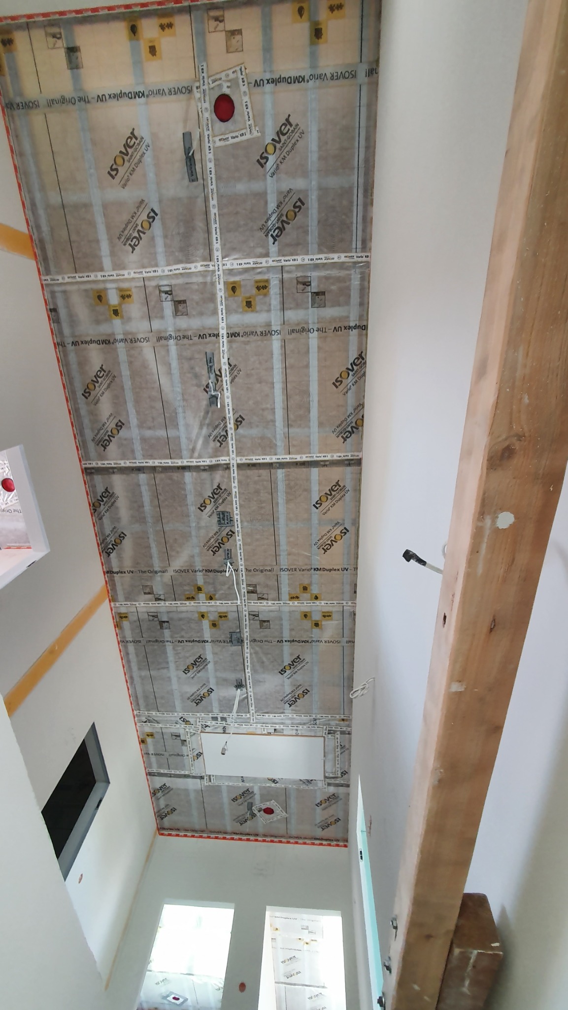 Izolacja poddasza z folią paroizolacyjną Isover Vario KM Duplex UV, widok z dołu. Układanie izolacji, widoczne elementy konstrukcyjne i instalacje.