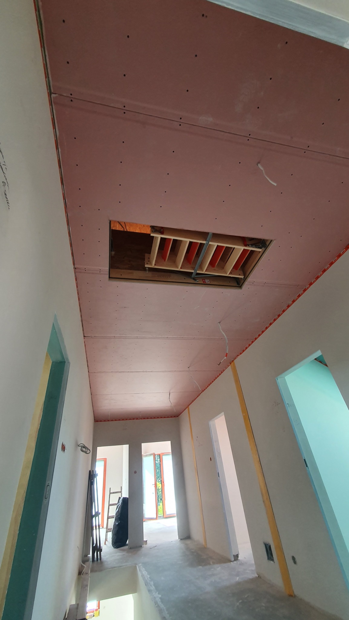 Sufit z płyt gipsowo-kartonowych, widoczne łączenia i otwór rewizyjny z elementami konstrukcyjnymi. Ściany przygotowane do dalszych prac wykończeniowych. Surowy stan wnętrza.