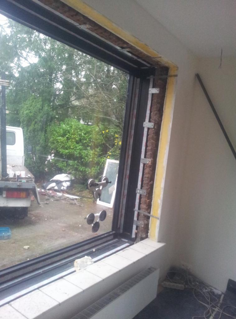 Montaż okna: widok od wewnątrz na okno w trakcie instalacji, z widocznymi elementami mocującymi, przyssawkami do szkła i fragmentem otoczenia zewnętrznego.