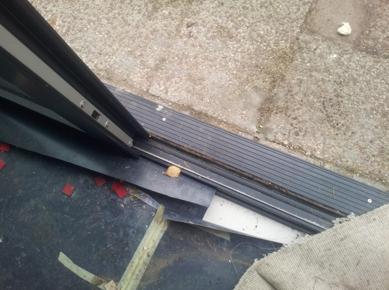 Fragment montażu bramy garażowej z widoczną szyną prowadzącą, elementami mocującymi i drobnymi odpadkami. Ujęcie z bliska, z góry.