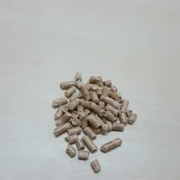 Jasne pellety drzewne ułożone w stos na drewnianym blacie, z widocznym fragmentem dokumentu po prawej stronie kadru. Widok z góry.