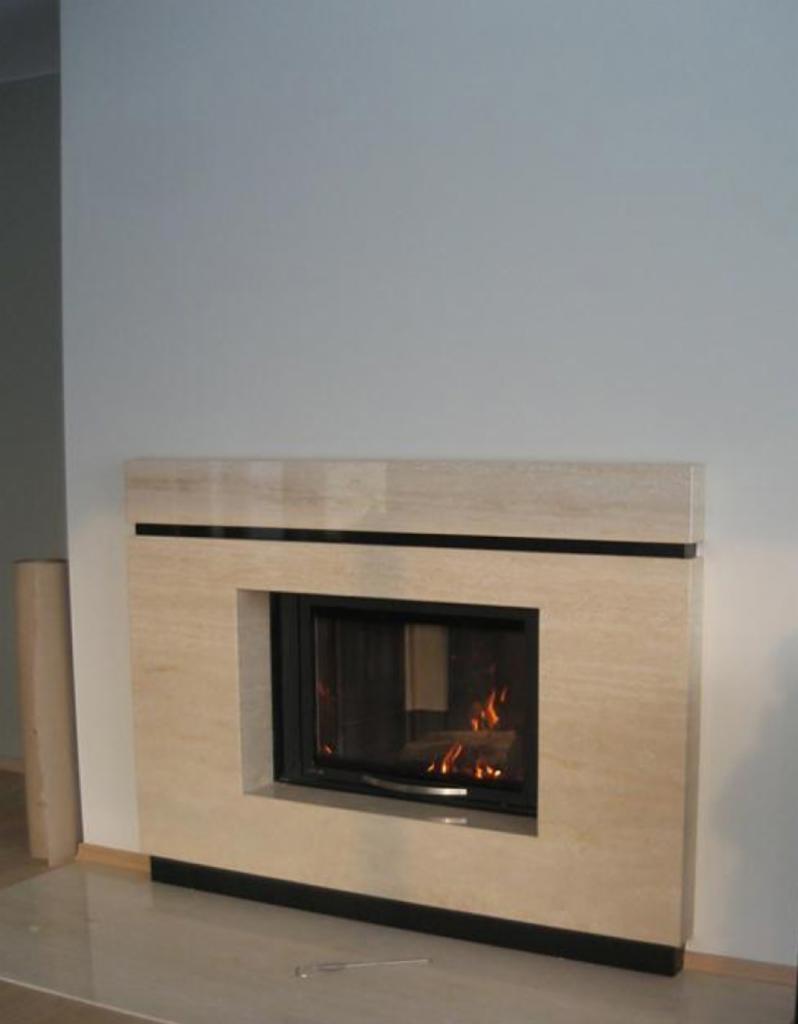 Elegancki kominek z beżowego kamienia z czarnymi akcentami, płomienie widoczne przez szybę, minimalistyczny design w nowoczesnym wnętrzu.