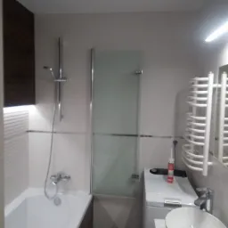 Nowoczesna łazienka z wanną, szklanym parawanem nawannowym, umywalką nablatową i pralką, wykończona w jasnych kolorach z akcentami drewna.