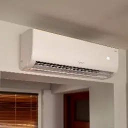 Zamontowany klimatyzator Rotenso na białej ścianie w pomieszczeniu z drewnianymi żaluzjami i drzwiami.