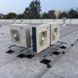 Instalacja trzech jednostek zewnętrznych klimatyzacji marki Daikin na płaskim dachu w Rybniku, zamontowanych na specjalnej konstrukcji wsporczej z czarnymi podstawami, widok na odległe budynki...