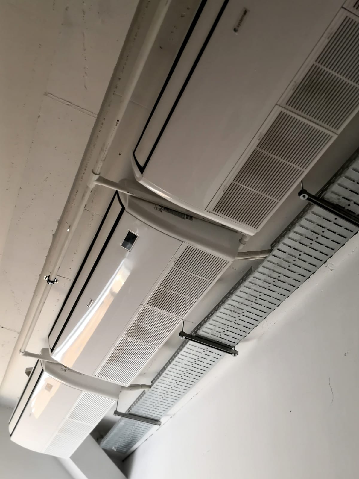 Sufit z zamontowanymi jednostkami klimatyzacji kasetonowej i metalowymi korytkami kablowymi, widok z dołu.