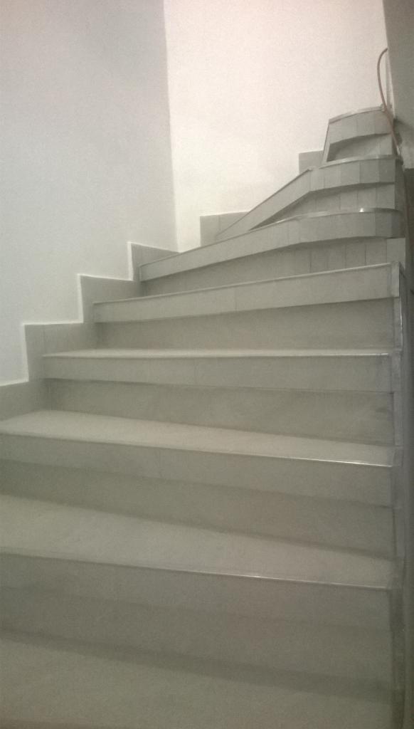 Schody wewnętrzne wyłożone jasnoszarymi płytkami ceramicznymi, prowadzące w górę, z widocznymi detalami wykończenia i gładką powierzchnią stopni.