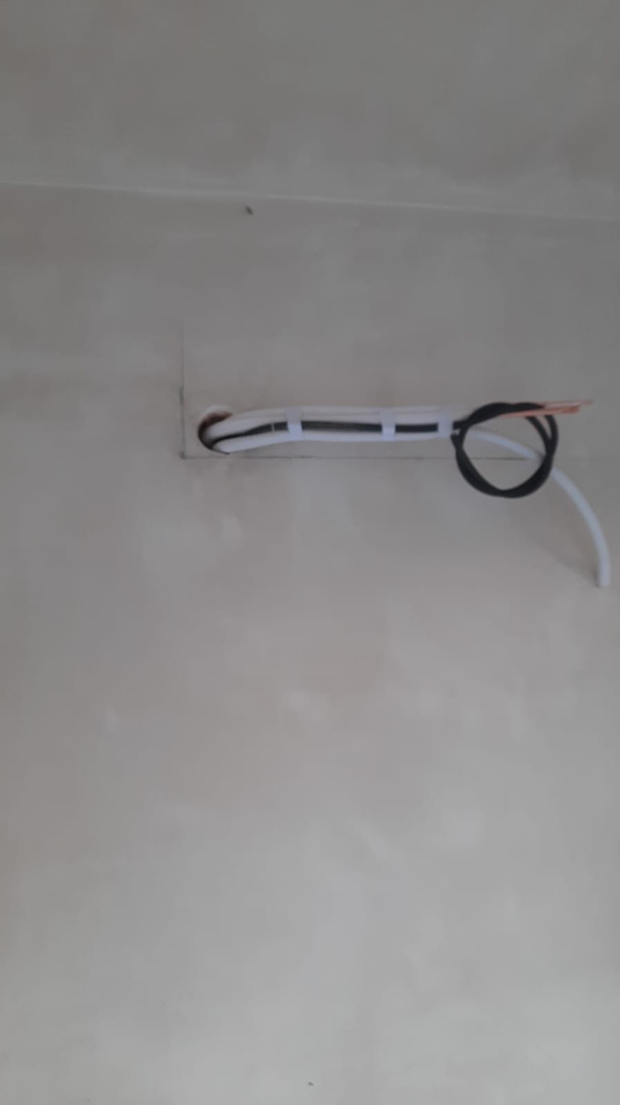 Białe i czarne kable klimatyzacji wychodzące z otworu w jasnej ścianie, zabezpieczone taśmą.