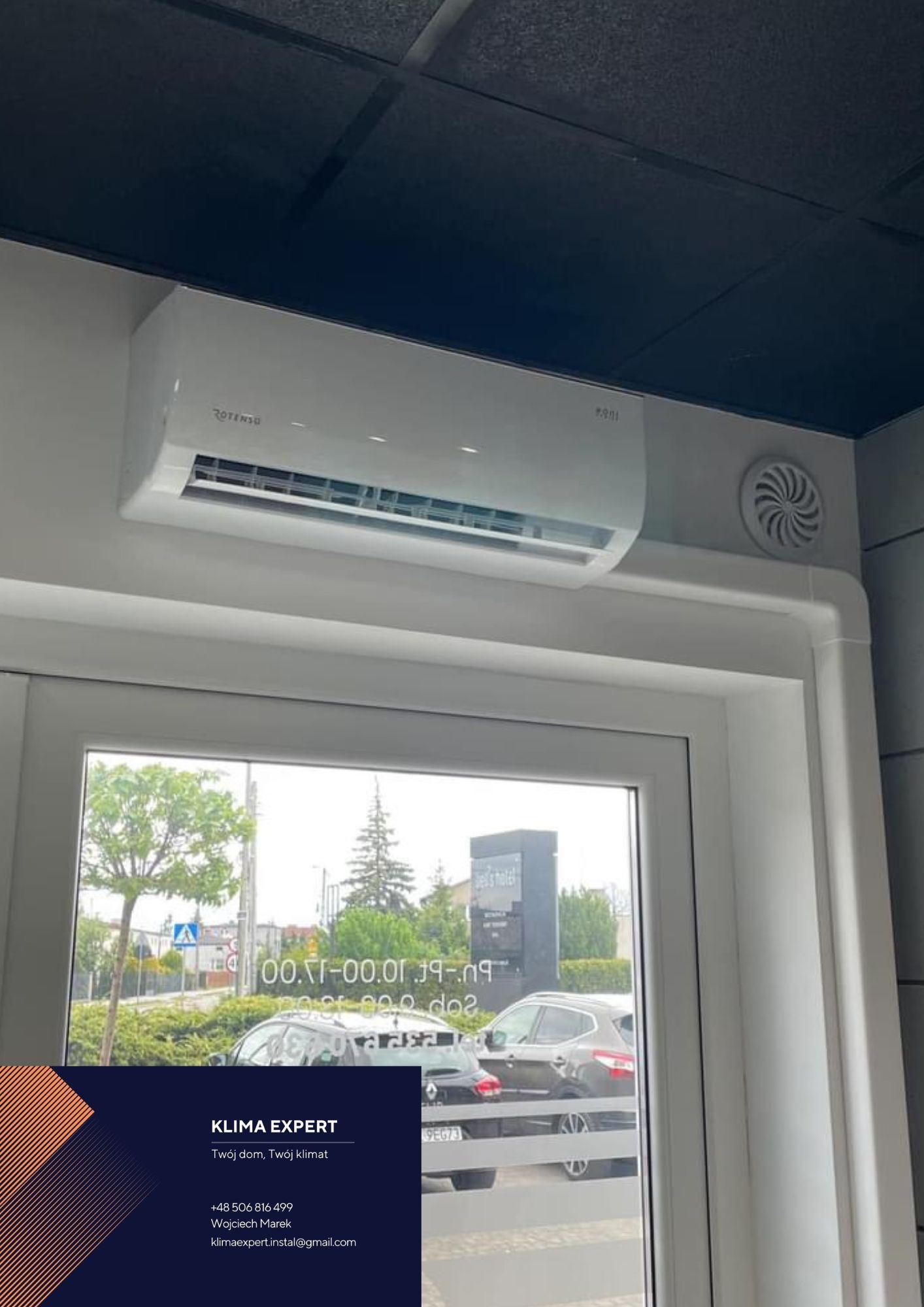 Biały klimatyzator Rotenso zamontowany nad oknem, widoczny nawiewnik obok urządzenia i odbicie ulicy w szybie okiennej.