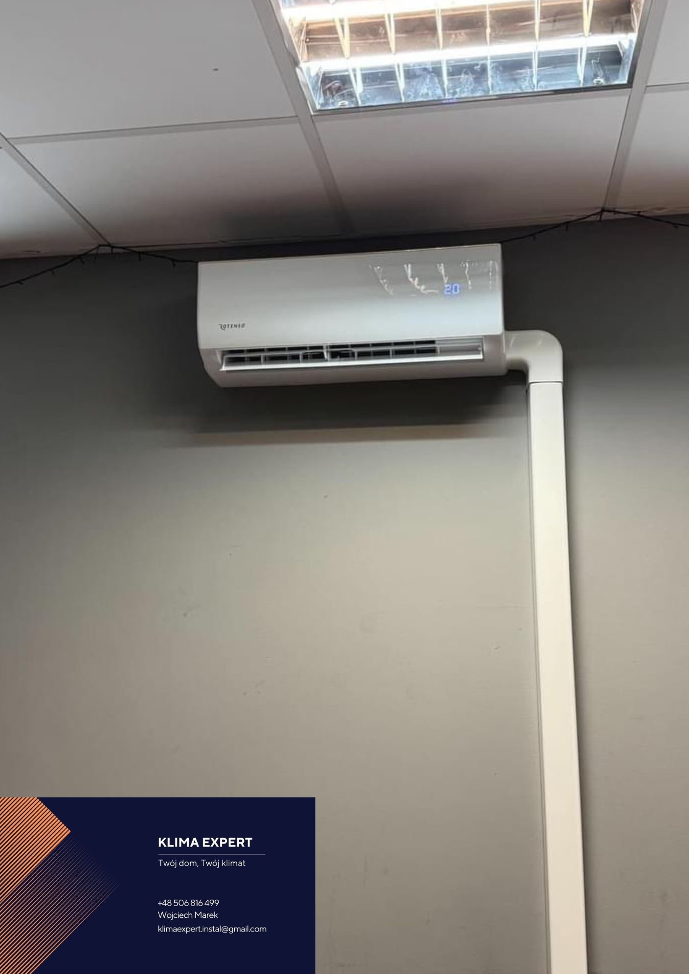 Zamontowany klimatyzator Rotenso na szarej ścianie w pomieszczeniu z podwieszanym sufitem, widoczna biała rura odprowadzająca skropliny i wizytówka firmy Klima Expert w lewym dolnym rogu.