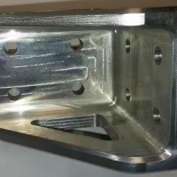 Precyzyjnie obrobiony, aluminiowy element kątowy z otworami i trójkątnym wycięciem, widoczne ślady obróbki skrawaniem.