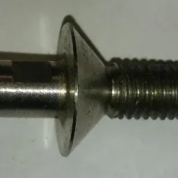 Metalowy trzpień z gwintem i stożkową główką, widoczne ślady obróbki i drobne zarysowania na powierzchni.