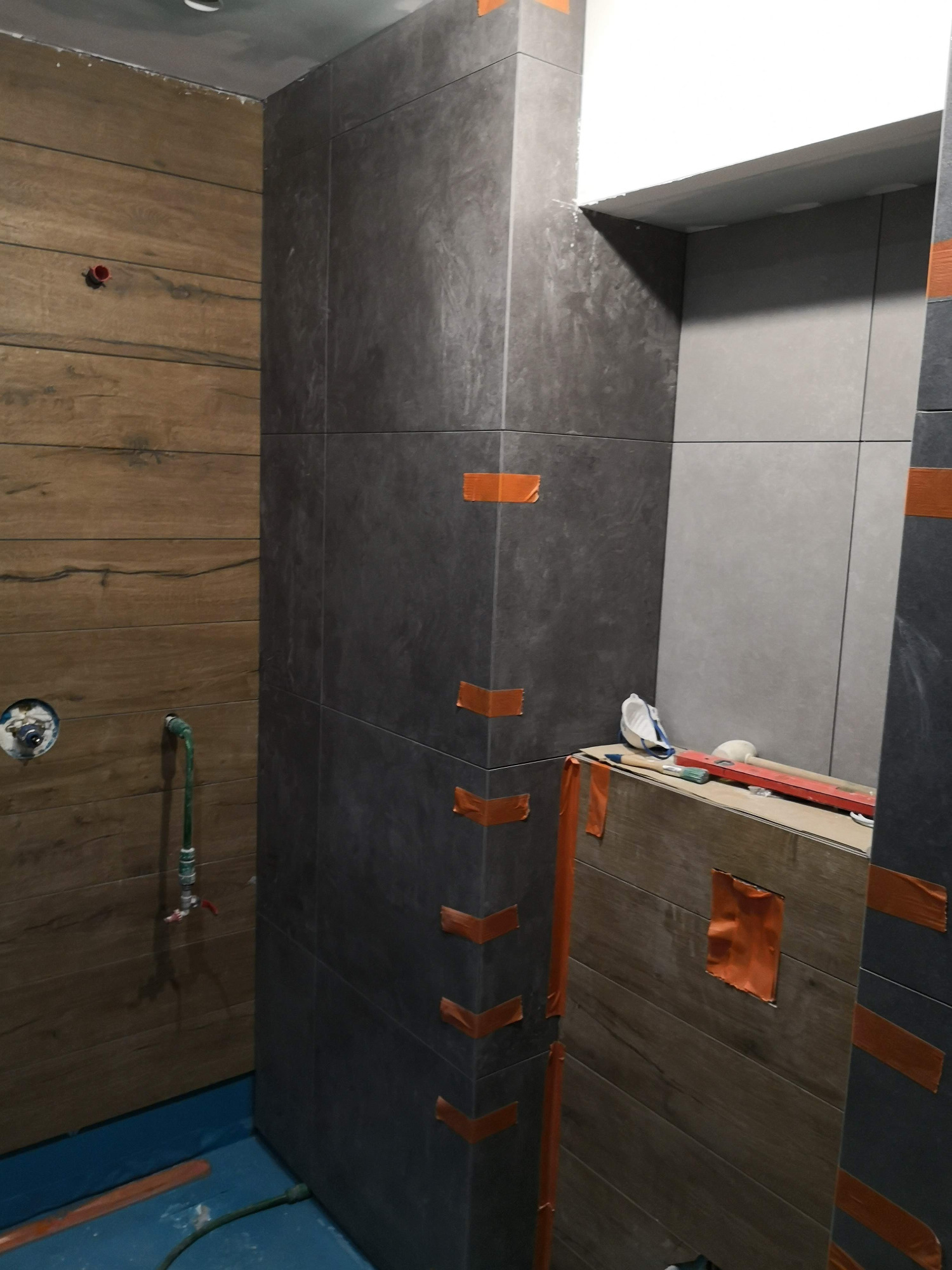 Układanie płytek imitujących drewno i grafitowych w kabinie prysznicowej w Brzeźnicy, zabezpieczone taśmą malarską, widoczne narzędzia i poziomica.